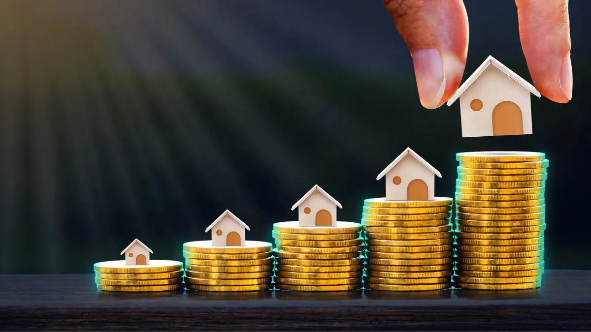 weirdwealth.io | 30 Money Habits Worth Copying From Wealthy Business Owners Hand placing a model house on the tallest stack of gold coins.